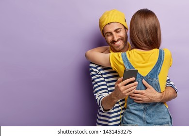 Glad Male Cheater Sends Text Message To Lover While Embraces Wife, Has Secret Chat Behind Girlfriends Back, Holds Modern Cell Phone In Hand, Ignores Live Communication. Marriage, Relationship Concept