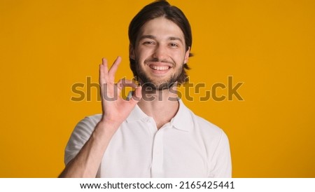 Glad man showing okay gesture and approval sign giving positive reply against orange background. Attractive guy asserting everything is ok over colorful background
