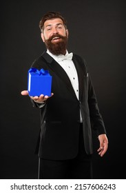 Glad Man In Tuxedo Bow Tie Formalwear On Black Background With Gift Box. Boxing Day