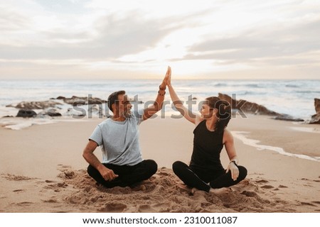 Glad mature european woman and man in sportswear practice yoga, give high five, enjoy workout together in morning on sea beach, outdoor. Teamwork for sports, fitness and body care