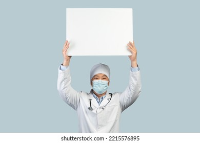 Glad Mature Japanese Male Worker In White Coat, Protective Mask Show Banner With Blank Space, Isolated On Blue Background, Studio. Protest, Agitation, Health Care, Medicine And Treatment, Offer And Ad