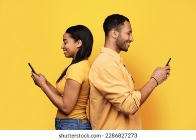 Glad millennial african american guy and female typing on smartphone, surfing in internet, isolated on yellow studio background, profile. Chat in social networks, device for communication - Powered by Shutterstock