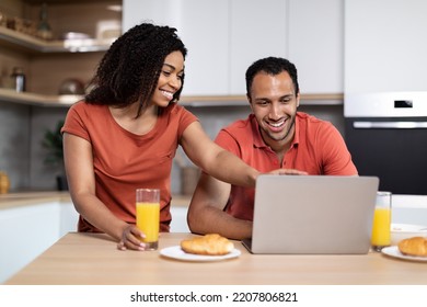 Glad Millennial Black Family Enjoy Breakfast In Morning Together, Lady Pointing Finger At Laptop In Kitchen Interior. Device To Video Call, Meeting Remotely, Ad And Offer, Work And Business At Home