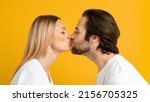Glad millennial european guy and woman in white t-shirts kiss and enjoy tender moment together, isolated on yellow background, close up, studio, profile. People, love, family relationship and ad