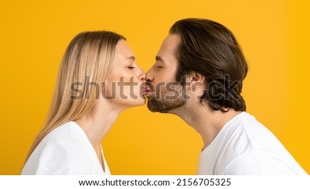 Glad millennial european guy and woman in white t-shirts kiss and enjoy tender moment together, isolated on yellow background, close up, studio, profile. People, love, family relationship and ad