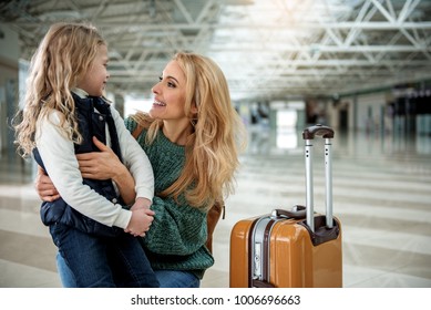 Glad Mom And Daughter Saying Goodbye Each Other At The Airport. Kid Is Taking Seat On Her Knee And Smiling