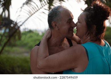 Glad, nice, lovely senior couple of woman and man hugging and rubbing noses in tropical forest, jungle on sky back view. Walking and dating, romantic tropical resort for tourists. Anniversary holiday - Powered by Shutterstock