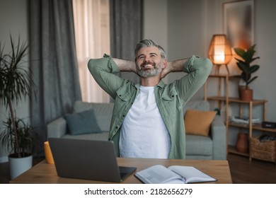 Glad Old European Man With Beard Take Break At Workplace With Laptop, Rest At Free Time In Living Room Interior. Work Remotely, Relax And Rest, Successful Business At Home During Covid-19 Pandemic