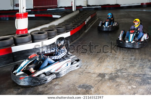 Glad people in helmets driving cars for karting in\
sport club indoor