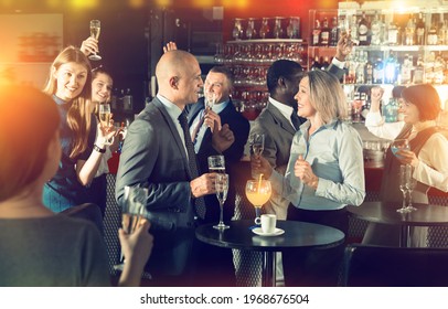 Glad positive middle aged woman with male colleague enjoying office party in bar, talking and toasting with drinks - Powered by Shutterstock