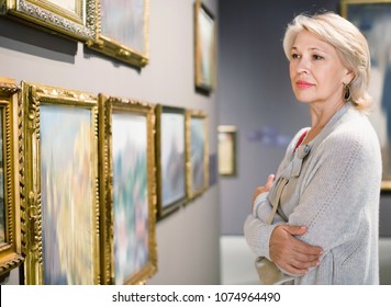Glad  positive smiling female visitor looking at artwork painting in the museum indoors