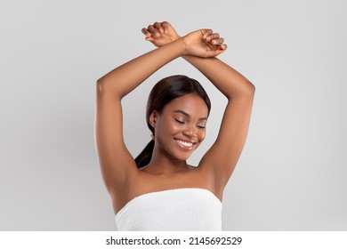 Glad Pretty Millennial Black Lady With Perfect Skin In Towel Raises Hands Up Show Armpits, Isolated On Gray Background. Hair Removal, Deodorant, Beauty And Body Care, Hygiene, Routine Procedures