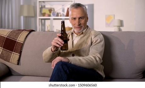 Glad retired male toasting beer bottle relaxing at home sofa, alcohol drink - Powered by Shutterstock