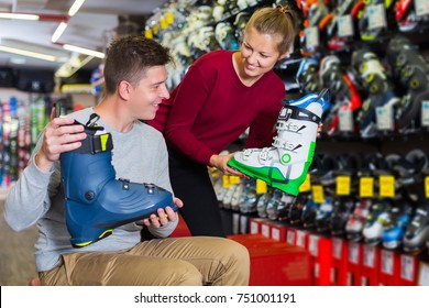 Glad seller woman is helping male to trying on ski boots in sport shop.
