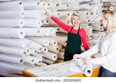 Glad Senior Woman Seller Displaying Diverse Fabrics To Young Customer In Textile Shop