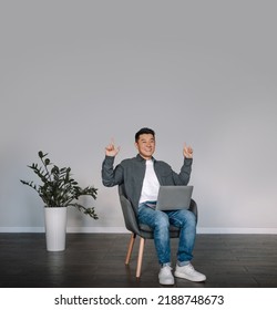 Glad Smiling Middle Aged Chinese Male With Laptop Making Victory Gesture With Hands Sit In Armchair In Room Interior. Entertainment With Device Alone At Home, Success Work, Great Offer, Ad And Win