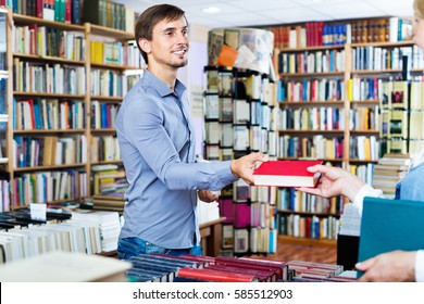 Glad Smiling Positive Man Taking Chosen Book From Seller In Book Shop