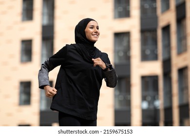 Glad smiling young arab female in hijab with fitness tracker running on building background outdoor. Fitness outside, jogging in morning, body and health care, training, ad and great sports offer - Powered by Shutterstock