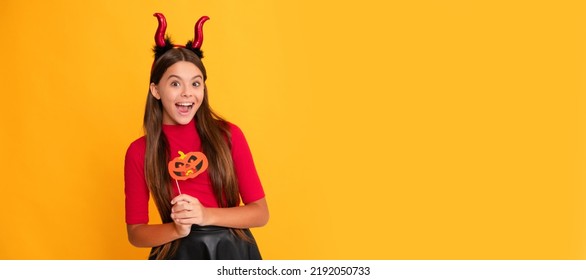 glad teen girl wearing imp horns holding pumpkin party accessory. Halloween kid girl portrait, horizontal poster. Banner header with copy space. - Shutterstock ID 2192050733
