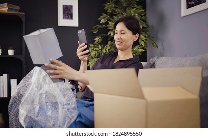 Glad Woman Holding Cellphone Taking Picture Of New Purchase After Unboxing Delivered Parcel At Home