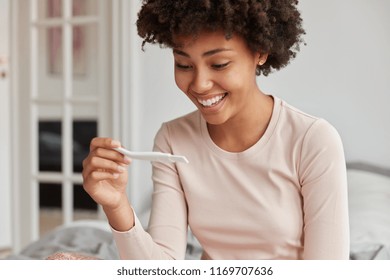 Glad Woman Looks At Pregnancy Test Has Cheerful Expression, Finds Out She Will Become Future Mother Soon, Going To Share Good News With Husband, Feels Excited With Positive Results. Maternity Concept