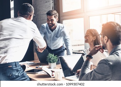 Glad to work with you! Young modern men in smart casual wear shaking hands and smiling while working in the creative office - Shutterstock ID 1099307402