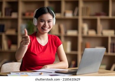 Glad Young Asian Woman With Down Syndrome In Headphones With Laptop Point Finger At Camera In Office Interior. Your Turn, Education At Home, Study And Social Distancing, Ad And Offer During Covid-19