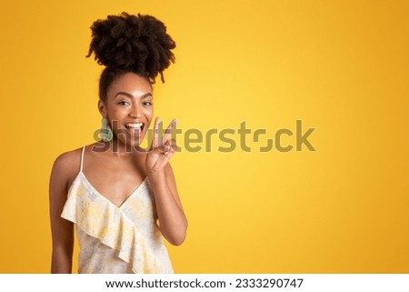 Glad young black woman in dress with open mouth making peace sign with hand, isolated on yellow background, studio. Lifestyle recommendation, good news gesture, fun emotions, ad and offer