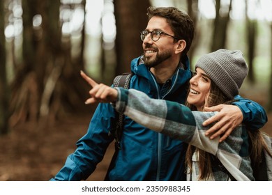 Glad young caucasian couple in jackets enjoy journey, points finger at copy space, rest in forest, outdoor, close up. Hiking, active lifestyle, adventure and tourism, people emotions - Powered by Shutterstock