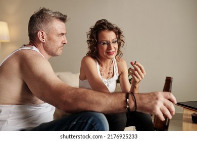 Glam rock mature couple smoking weed and drinking beer at home when watching show on laptop