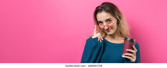 Glamor woman in glasses in a blue sweater with a drink of coffee on a pink background	 - Shutterstock ID 1600691758
