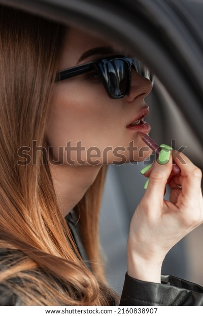 Glamorous\
beautiful young woman with fashion sunglasses with a pretty face\
and sexy lips draws makeup and sits in the car\
