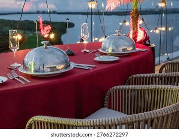 A glamorous close-up of a fine dining table setting featuring exquisite tableware, elegant glassware, and silver cloches, highlighting the luxury of the meal being prepared.