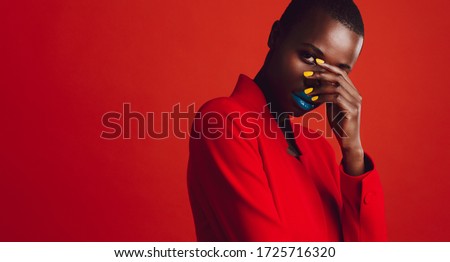 Glamorous female model on red background. African woman with buzz cut hairstyle and vibrant makeup looking at camera.