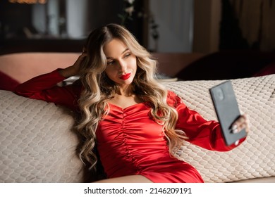 glamorous female in a red dress with makeup is photographed on the phone sitting on the couch	