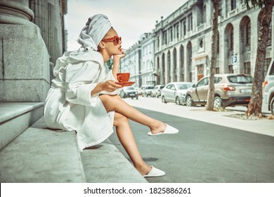 Glamorous Lifestyle. Stunning Woman In A White Terry Dressing Gown With A White Towel On Her Head And Elegant Sunglasses Alluring On A City Street With A Cup Of Tea And Cigarette. Fashion Shot. 