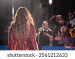 Glamorous model struts in shiny red ensemble on runway, captivating photographers at exclusive fashion event.