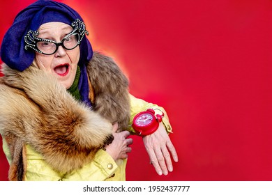 Glamorous Old woman wears an alarm clock like a wristwatch. Stylish older woman in turban and glamorous glasses. Grandma shows watch on her arm. Hurrying cheerful elderly fashionista. Emotional people - Powered by Shutterstock