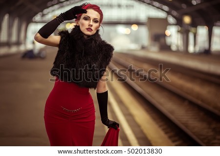 Glamorous retro girl at the train station in a red dress.Portrait of a beautiful girl. Vintage. Retro. Pin Up. Beautiful make-up and hairstyle in a classic style. Railway station. 