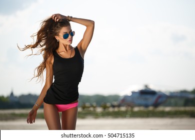 Glamorous, stylish girl of modeling appearance (skinny with thin waist) with waving loose hair is posing in lingerie on the runway wearing aviator sunglasses, stylish outdoor countryside  photoshoot