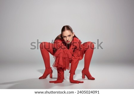 glamorous young model in red attire with high heels and bright tights posing on grey background