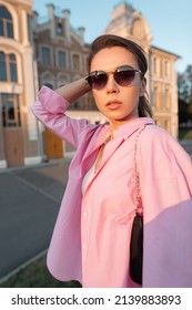 Glamorous Young Stylish Woman With Cool Sunglasses In A Trendy Pink Shirt And Gold Chain Purse Walks Outside On A Summer Sunny Day