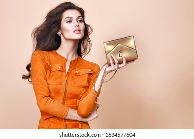 Glamour Beautiful Sexy Brunette Women, Looks Like A Model, Wearing Evening Make Up In Short Red Dress With Small Yellow Bag In Hands In Fashion Pose With Amazing Figure, Perfect Shape Girl Hairdo.