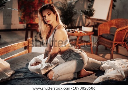 Glamour blond haired woman poses on a bed in comfortable and cosy room with bamboo furniture.