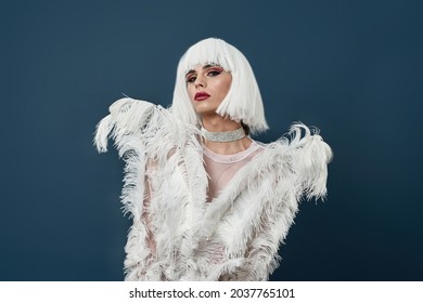 Glamour Drag Queen, Young Transgender With Bright Night Makeup Wearing Boa Feather Party Dress Looking At Camera, Posing Isolated Over Dark Blue Background. Beauty, Lgbtqi, Drag Show Concept