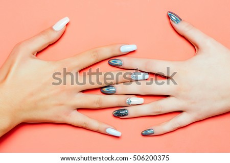 glamour female hands and fingers with fashionable trendy nail polish white and silver colors on fingernails has soft skin of young human on orange background, closeup