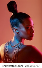 Glamour, jewelry and portrait of a model in a studio with neon lights for aesthetic and cosmetics. Makeup, art and young woman with cosmetic beauty routine with accesories posing by orange background