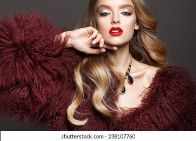 Potret glamor model wanita cantik dengan bibir merah dan rambut pirang panjang di mantel bulu mewah warna marsala Foto Stok