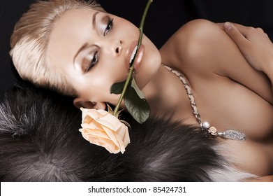 Glamour Shot Of A Sexy Blonde Laying On Black Wearing Fur And A Rose In Her Mouth