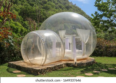 Glamping On Bali Beach, In Bubble House With Transparent Walls. White Wooden Double Bed With Mosquito Net Inside Bubble. Honeymoon In An Inflatable Tent. Tourist Attraction In Tropical Paradise.